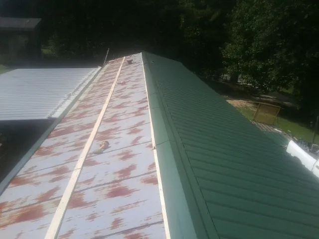 Old rusted panels beside newly installed green metal roofing — Wind Damage Roof Repair by Roofing Brothers in Henderson